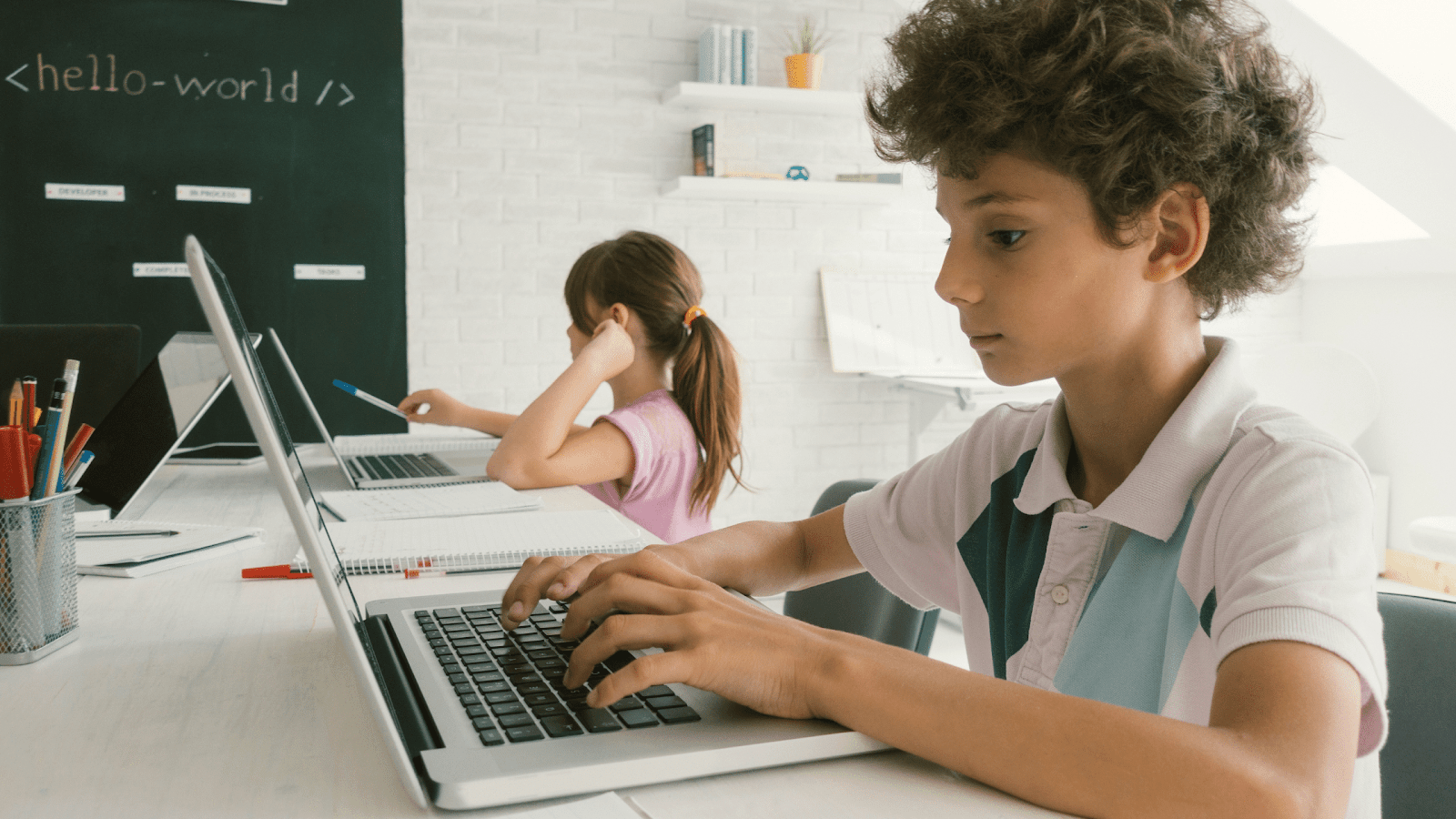 Boy coding at a laptop with girl coding in background